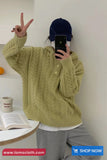 Person wearing a green cable knit sweater taking a selfie in a minimalistic room.