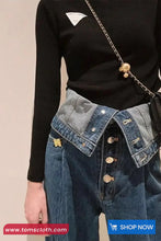 Person wearing a black long-sleeve top and blue denim jacket with gold buttons on a beige background.