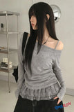 Woman wearing a gray off-shoulder top with a ruffled hem in an indoor setting.