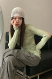 Person wearing a light green sweater and beige pants sitting on a chair.