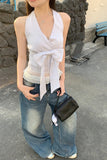 Woman wearing a white sleeveless top and blue jeans, holding a black handbag, standing on a stone pavement.