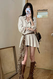 Woman taking a mirror selfie wearing a beige outfit with a leopard print scarf, brown boots, and a black handbag.