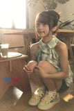 Young girl in a checkered dress sitting on the floor in a casual setting.