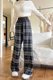 Person wearing a white sweater and plaid pants in a room with a couch and coat rack.