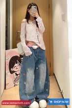 Person wearing a pink off-shoulder top and blue jeans with star designs, taking a mirror selfie.