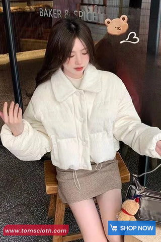 Woman wearing a white puffer jacket in a cafe setting with a teddy bear and 'Baker & Spice' sign.