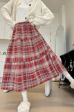 Person wearing a red plaid skirt with a white sweater and shoes in a room.
