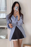 Woman taking a mirror selfie wearing a blue striped shirt and black skirt.