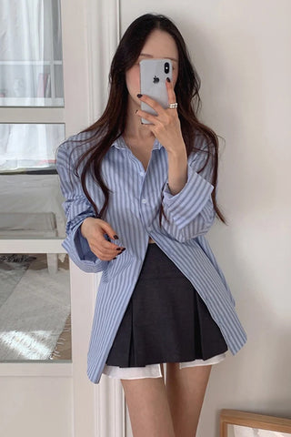 Woman taking a mirror selfie wearing a blue striped shirt and black skirt.