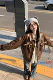 Person wearing a brown jacket and gray beanie with bear ears on a city street.