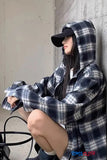Person wearing a plaid hoodie and cap sitting against a wall.