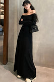 Woman wearing a black off-shoulder dress and cap, holding a black handbag against a neutral wall.