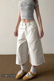 Person wearing a gray crop top and white wide-leg pants with 'Tomscloth' branding.