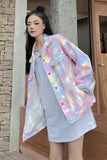 Woman wearing a pastel tie-dye jacket over a light dress, standing in front of a stone wall.