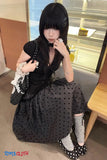 Woman in a black polka dot dress sitting on a chair indoors.