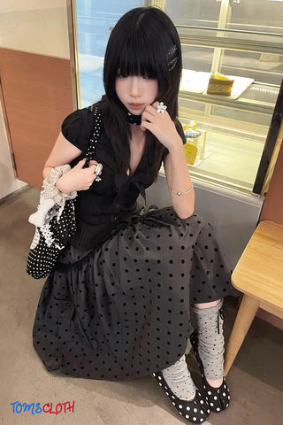 Woman in a black polka dot dress sitting on a chair indoors.