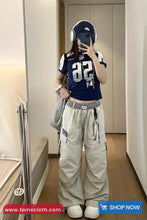 Person wearing a navy blue sports jersey with white lettering and light gray cargo pants, standing in a room.
