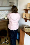 Person in a pink jacket standing in a kitchen with wooden shelves and a countertop.