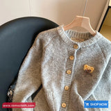 Children's cardigan with wooden buttons on a hanger against a neutral background