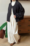 Person wearing a black cardigan, white shirt, and white pants in a room with wooden furniture.