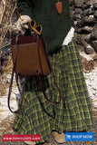 Person wearing a green plaid skirt and holding a brown leather bag with a stone wall background