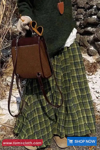 Person wearing a green plaid skirt and holding a brown leather bag with a stone wall background