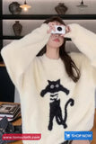 Person wearing a white sweater with a black cat design, holding a phone.
