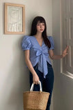 Woman in a blue top with a bow tie holding a woven basket, standing in a room.