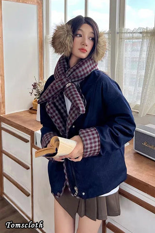 Woman wearing a navy blue coat with fur-lined hood and plaid scarf indoors.