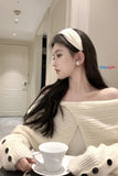 Woman in a white sweater holding a white cup in a room with a door and light fixture.
