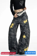Person wearing black camouflage pants with yellow stars and a black top on a white background.