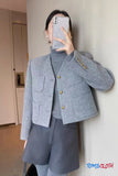 Person wearing a gray blazer with gold buttons in an indoor setting, holding a phone.
