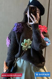 Person wearing a dark knitted sweater with colorful flower patterns, taking a mirror selfie.