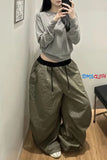 Person wearing a gray sweatshirt and beige pants, standing against a white wall.