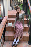 Woman sitting on a staircase wearing a green top and pink plaid skirt.