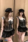 Woman wearing a black and white checkered top with ruffled details and a black skirt, standing against a wooden wall.