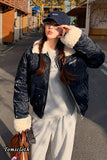 Woman wearing a dark blue puffer jacket with white fur lining, gray hoodie, and light gray pants on a street.