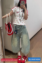 Person wearing a white shirt with red accents, blue jeans, and red shoes, holding a red and white bag.