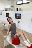 Woman sitting on a bench with a red handbag in a room with white walls and tiled floor.