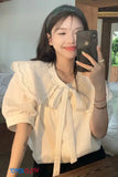 Woman taking a mirror selfie wearing a white blouse with lace details.