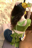 Woman in green top and denim shorts with a yellow flower in her hair, sitting on a brown surface.