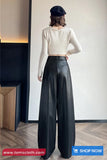 Person wearing a white long-sleeve top and black wide-leg pants in an indoor setting.