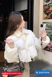 Woman in a white puffer jacket taking a selfie in a store.