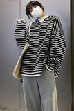 Person wearing a black and white striped sweater and gray pants, holding a beige bag.