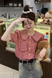 Person wearing a red checkered shirt and denim shorts, holding a teddy bear in a casual setting.