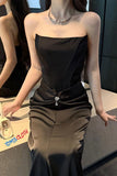 Woman wearing a black strapless dress with a silver embellishment, standing indoors.