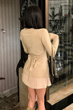 Woman wearing a beige dress with a pleated skirt and sweater in an indoor setting.
