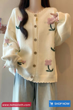 Cream-colored cardigan with floral patterns worn by a person against a neutral background.