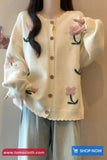Cream-colored cardigan with floral patterns worn by a person against a neutral background.