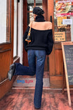 Person in black off-shoulder sweater and blue jeans standing in front of a store entrance.